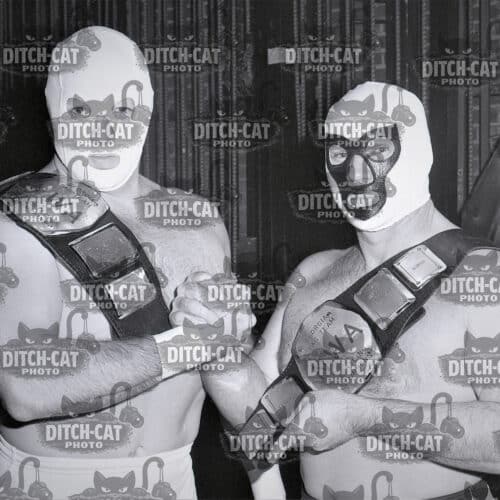 Two masked wrestlers pose with championship belts in a black-and-white photo.