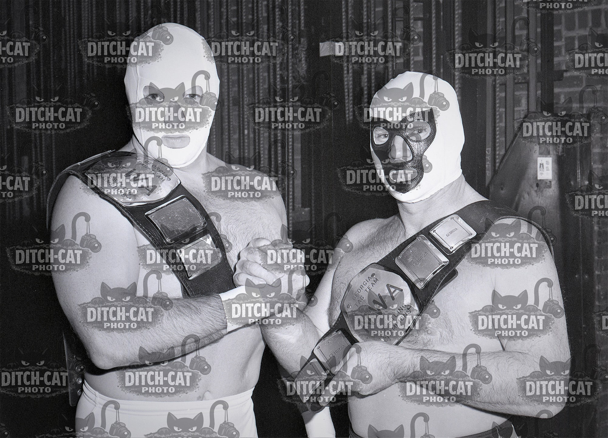 Two masked wrestlers pose with championship belts in a black-and-white photo.